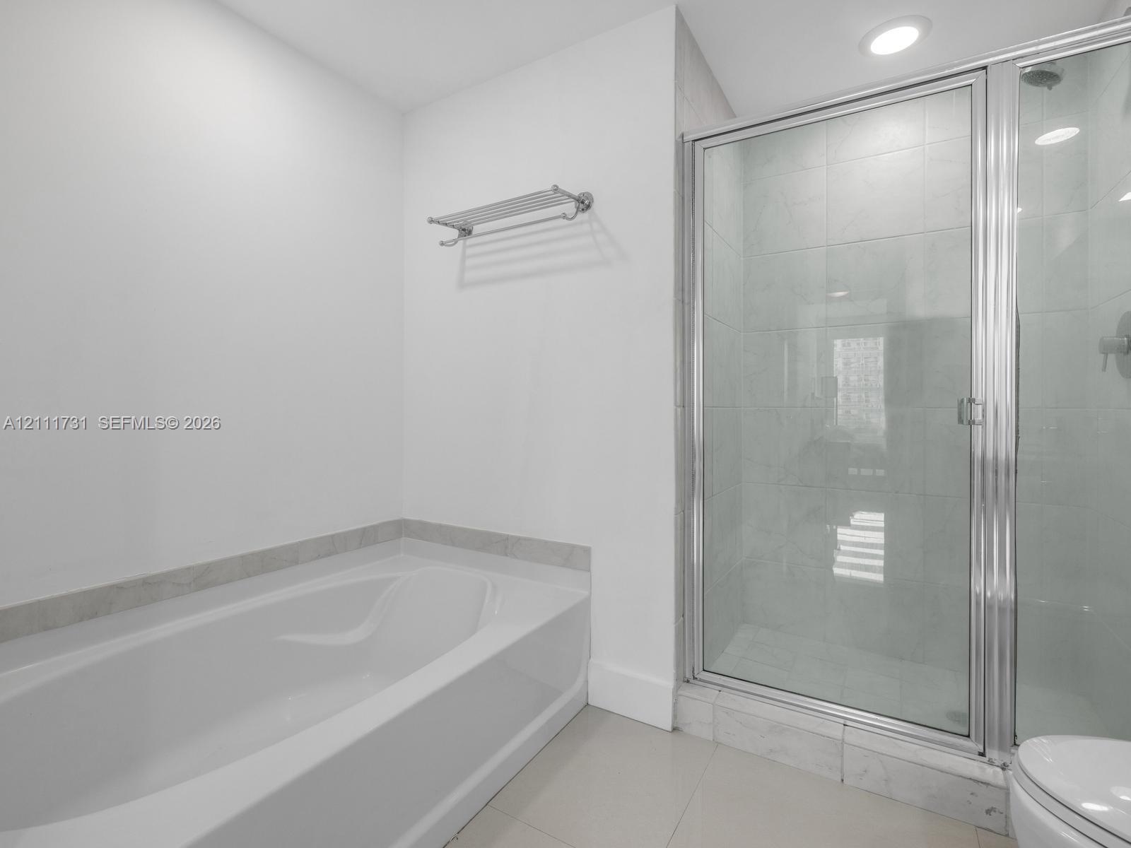 Bathroom featuring a deep soaking tub, separate glass-enclosed shower with tile surround, and built-in wall shelf