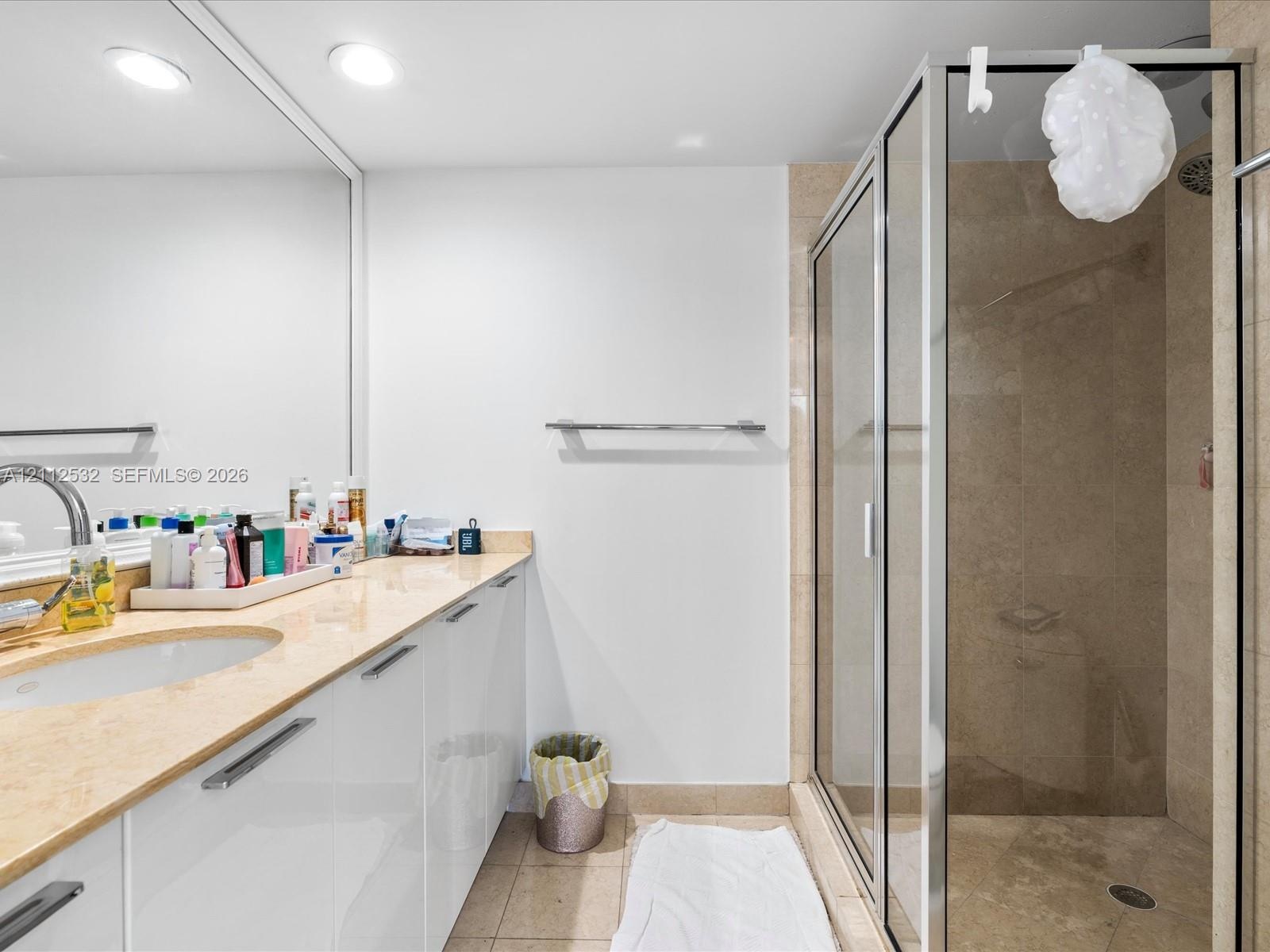 Bathroom featuring a wide vanity with high-gloss white cabinetry, a stone-surfaced countertop, a wall-to-wall mirror, and a walk-in shower enclosure w