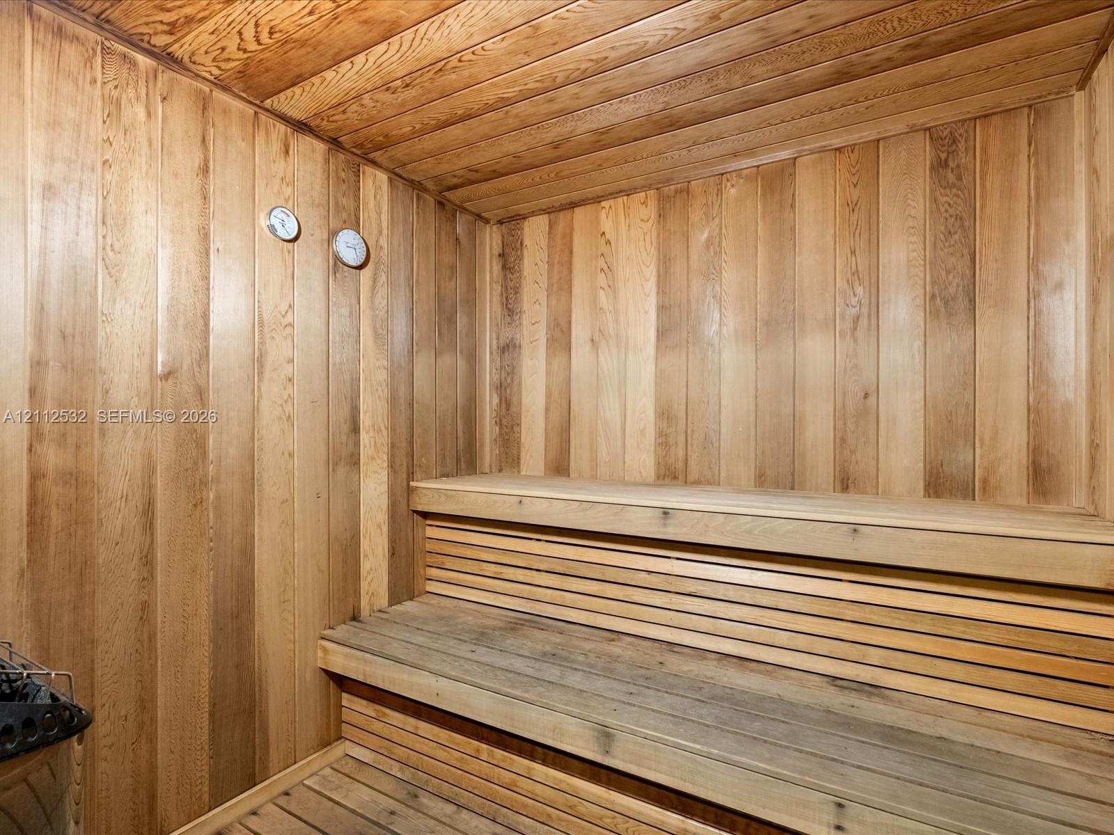 Sauna featuring natural wood-paneled walls and ceiling, tiered wood benches, and integrated wall-mounted analog gauges
