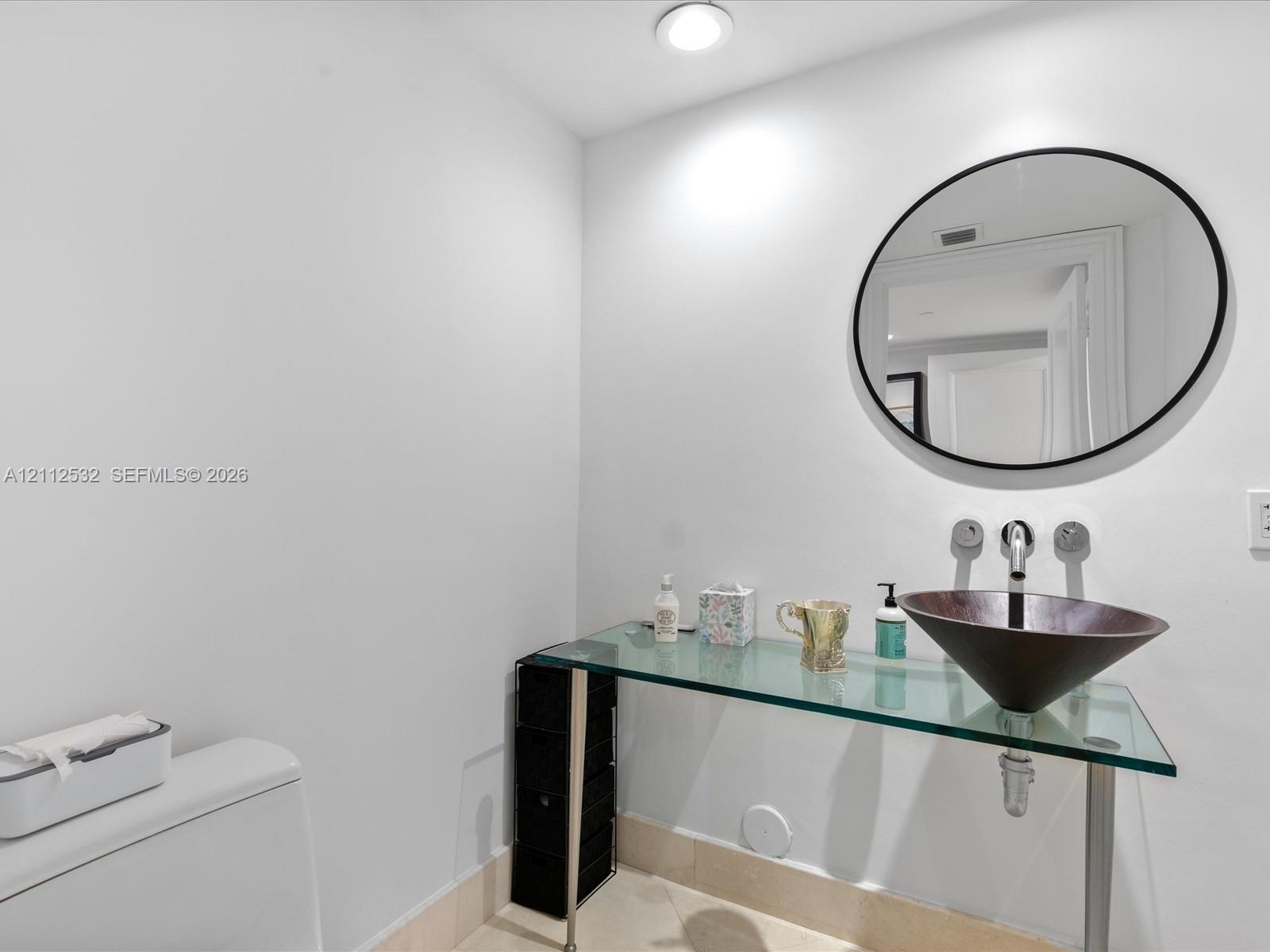 Glass-topped vanity featuring a conical vessel sink, wall-mounted faucet, and minimalist circular mirror
