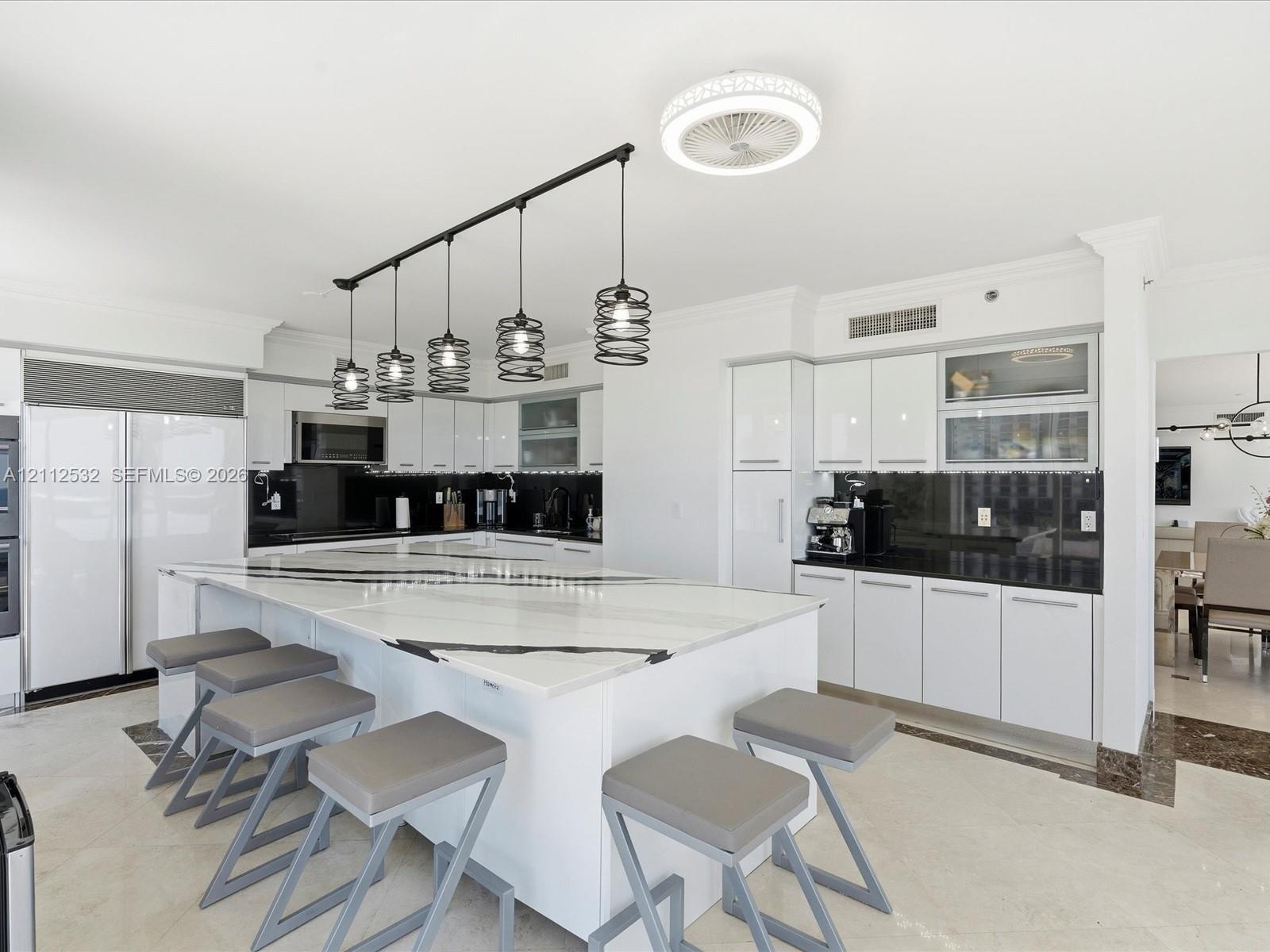 Kitchen featuring a large waterfall-edge island, high-gloss white cabinetry, contrasting dark stone countertops, integrated stainless steel appliances