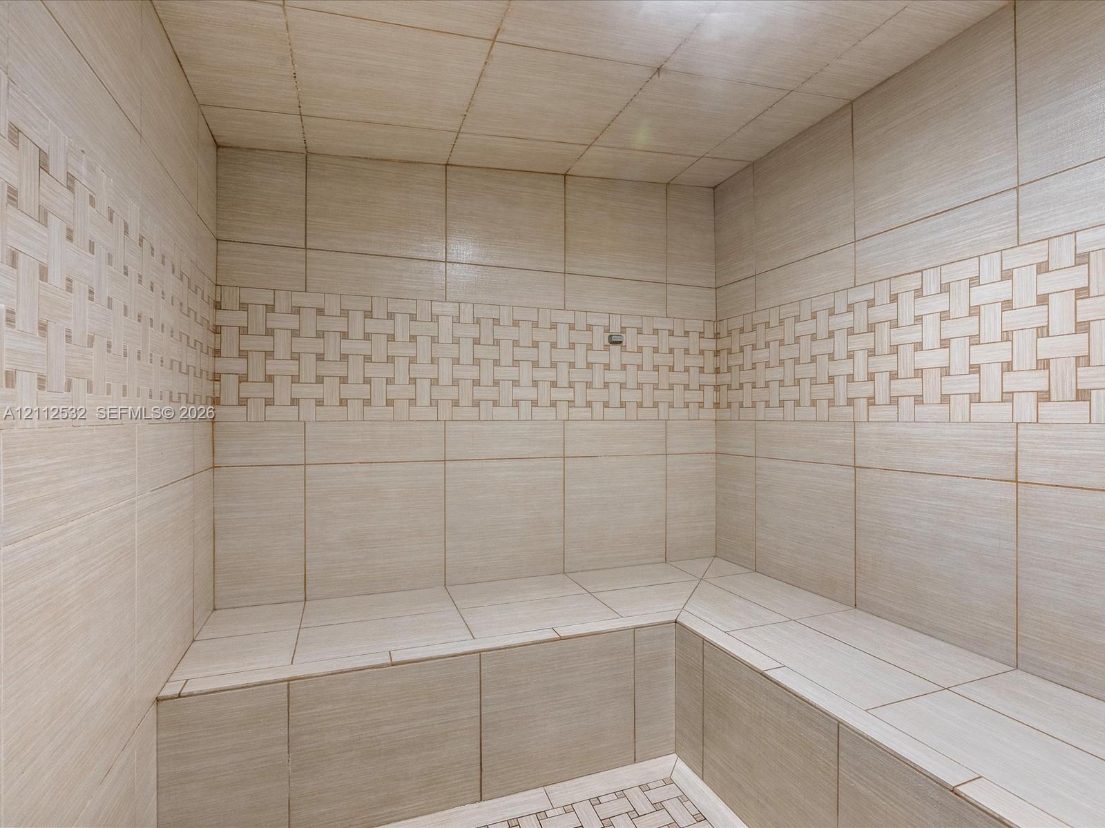 Tiled steam shower featuring built-in bench seating, large-format wall tiles, and decorative basket-weave accent detailing