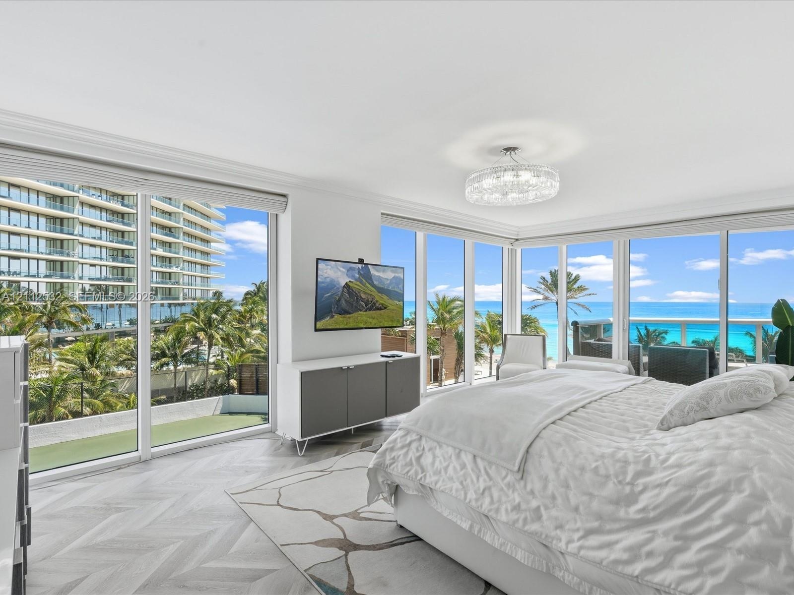 Floor-to-ceiling windows, herringbone-patterned wood-finish flooring, recessed crown molding, and a crystal-accented drum chandelier