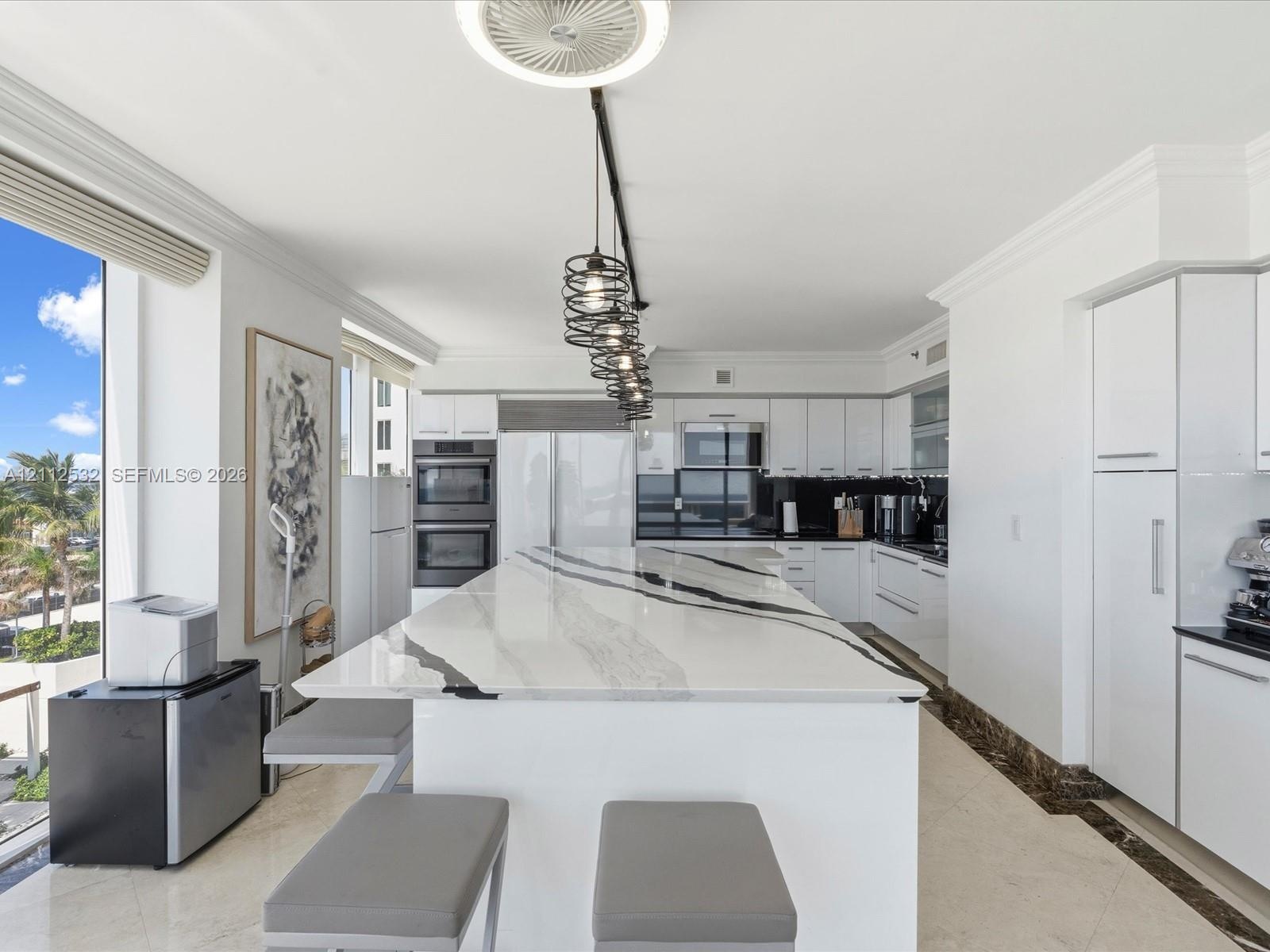 Kitchen featuring a substantial waterfall-edge island with stone countertop, flat-panel white cabinetry, built-in stainless steel appliances, multi-pe