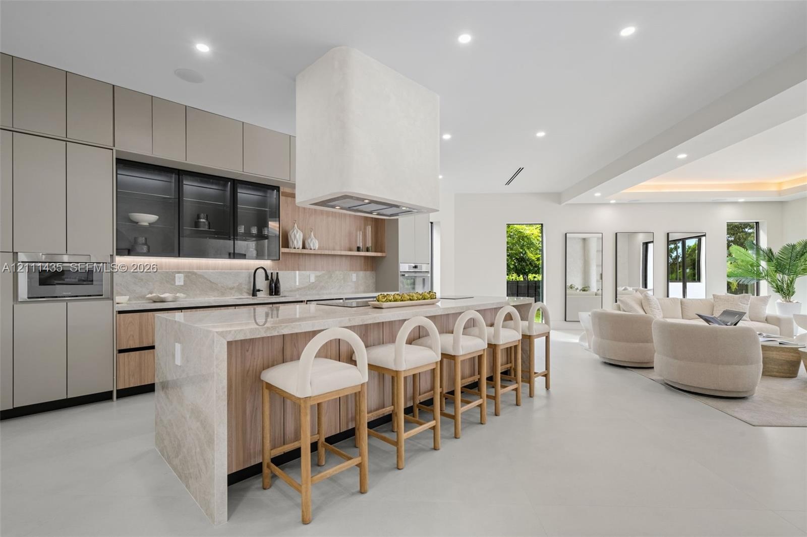 Modern kitchen featuring matte-finish cabinetry, a waterfall-edge stone island, integrated oven and microwave, recessed lighting, and a custom plaster