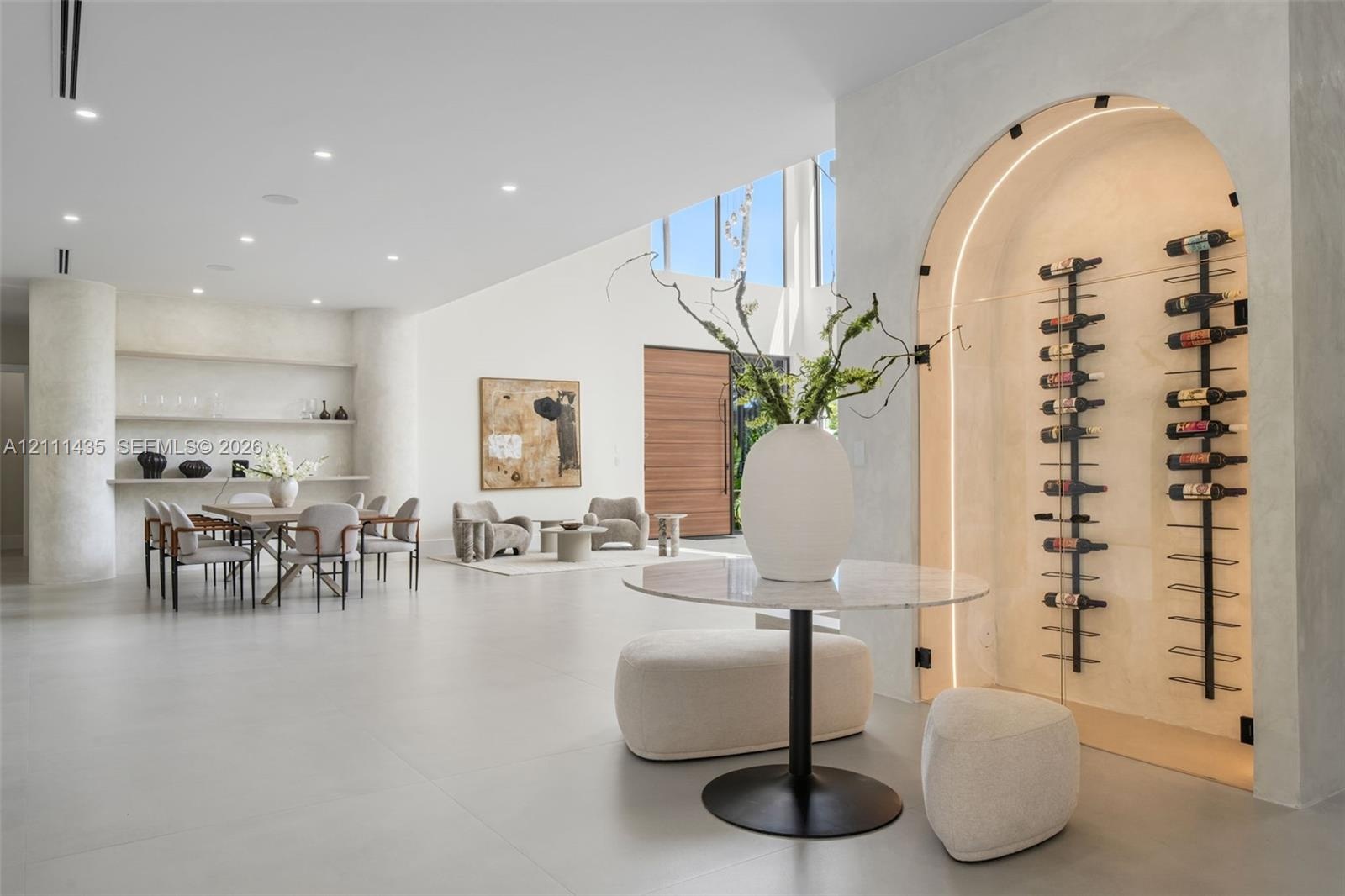 Arched, climate-controlled glass wine display with integrated accent lighting, built-in shelving, smooth plaster wall finishes, recessed ceiling light