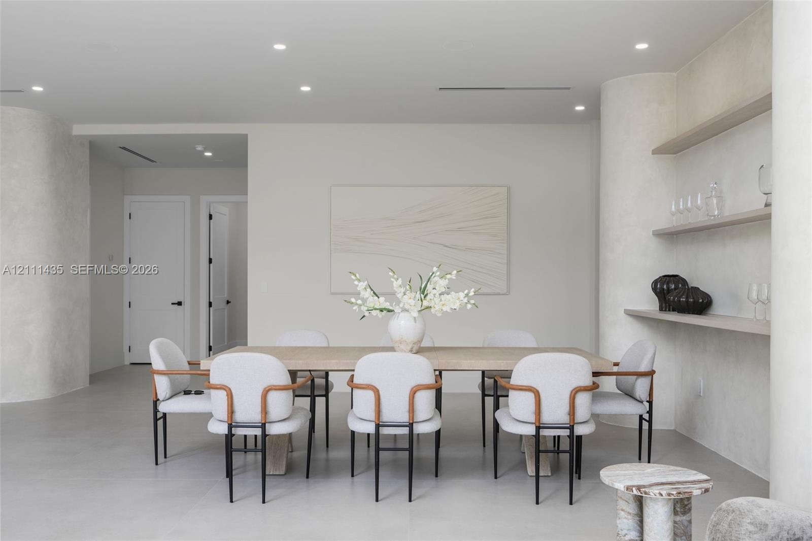 Interior space featuring smooth plaster wall finishes, curved structural columns, integrated wall shelving, recessed ceiling lighting, and solid-core 