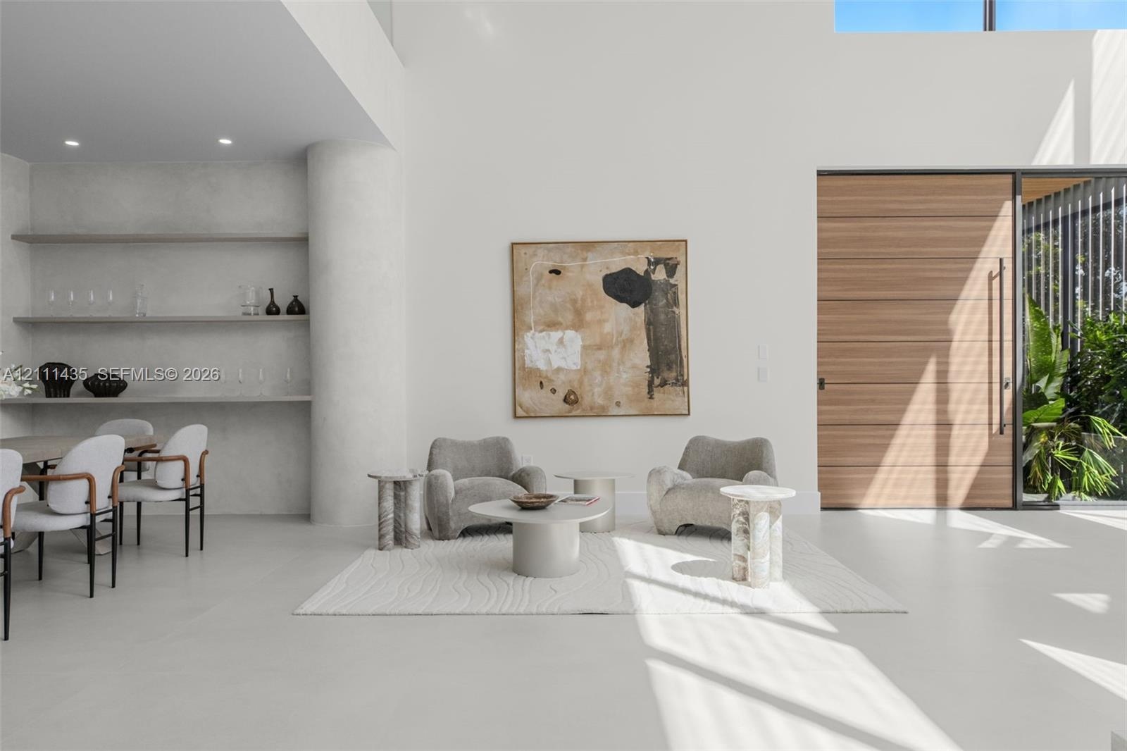 Double-height ceiling with recessed lighting, integrated stone shelving, polished concrete flooring, oversized wood-finish front entry door, and floor