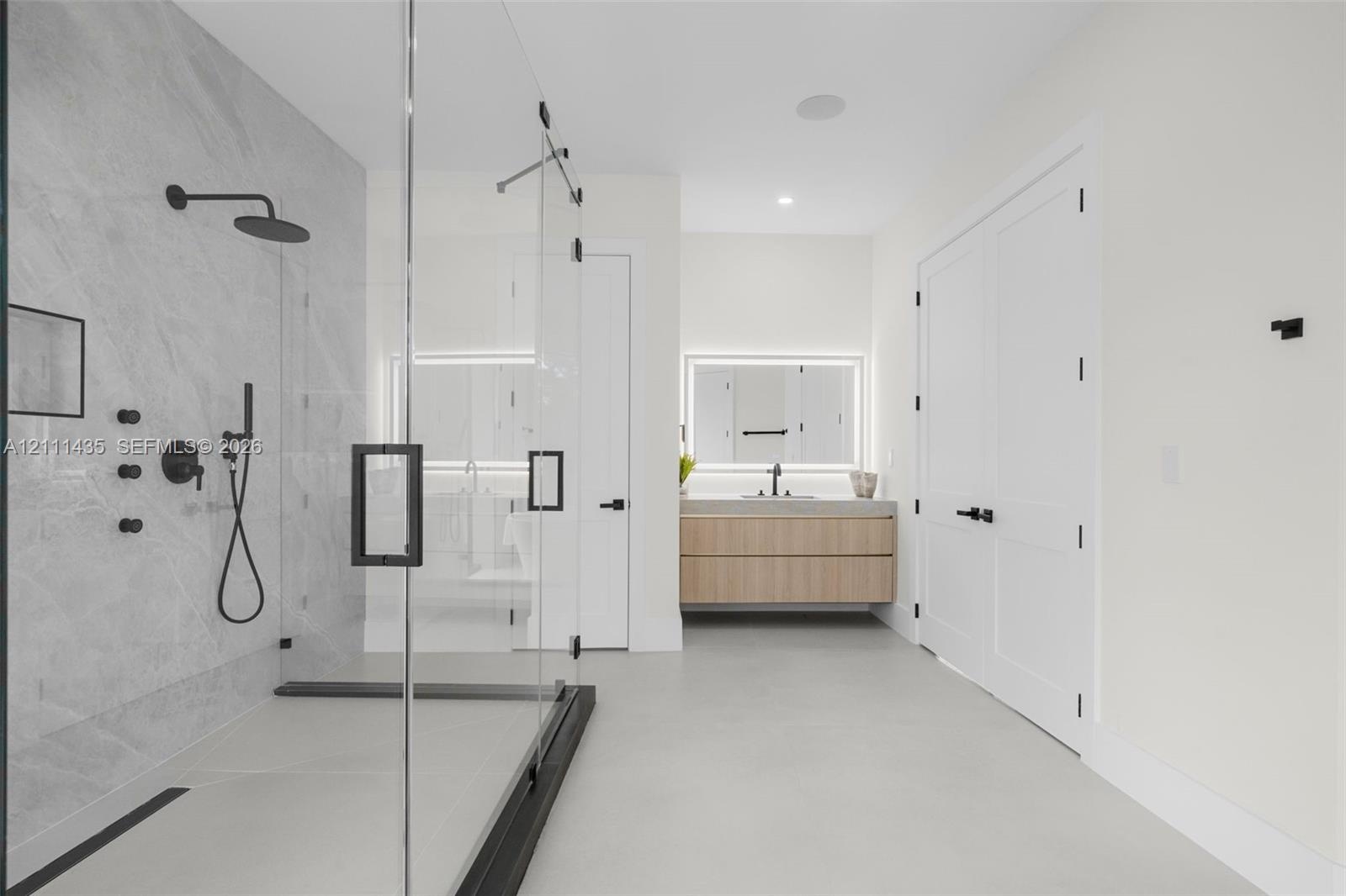 Walk-in shower with frameless glass enclosure, rainfall shower head, and stone-tile surround, paired with a floating wood-finish vanity featuring an i
