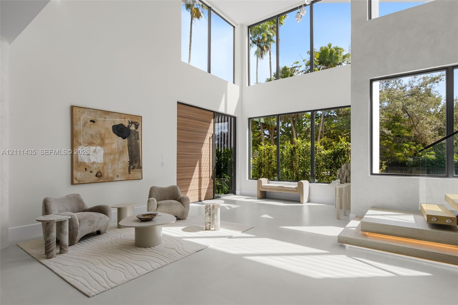 Double-height living area featuring floor-to-ceiling windows, polished concrete flooring, a natural wood entry door, and a floating staircase with int