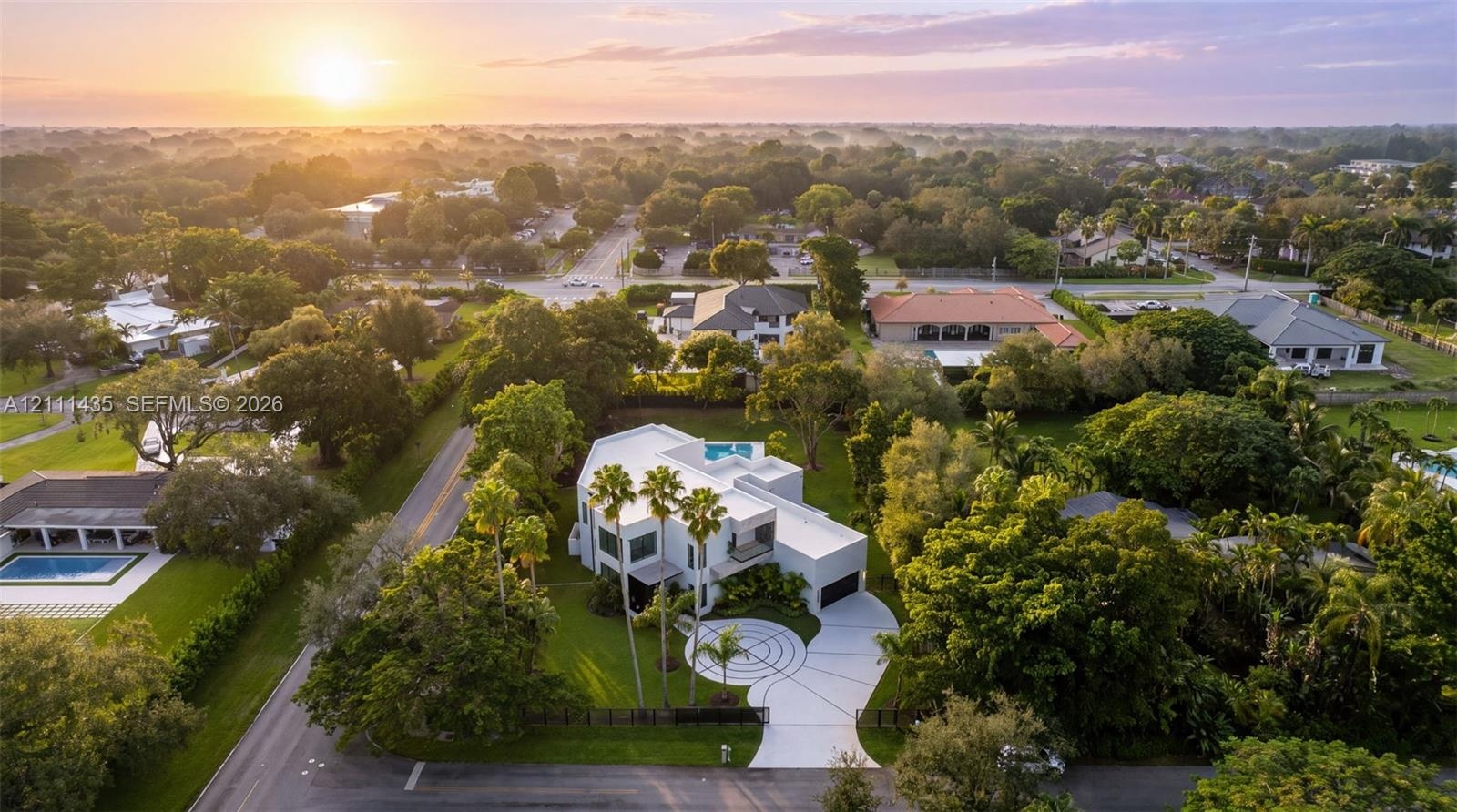 Aerial perspective of a multi-level contemporary residence featuring a flat roofline, circular concrete driveway, private rooftop pool, and mature per