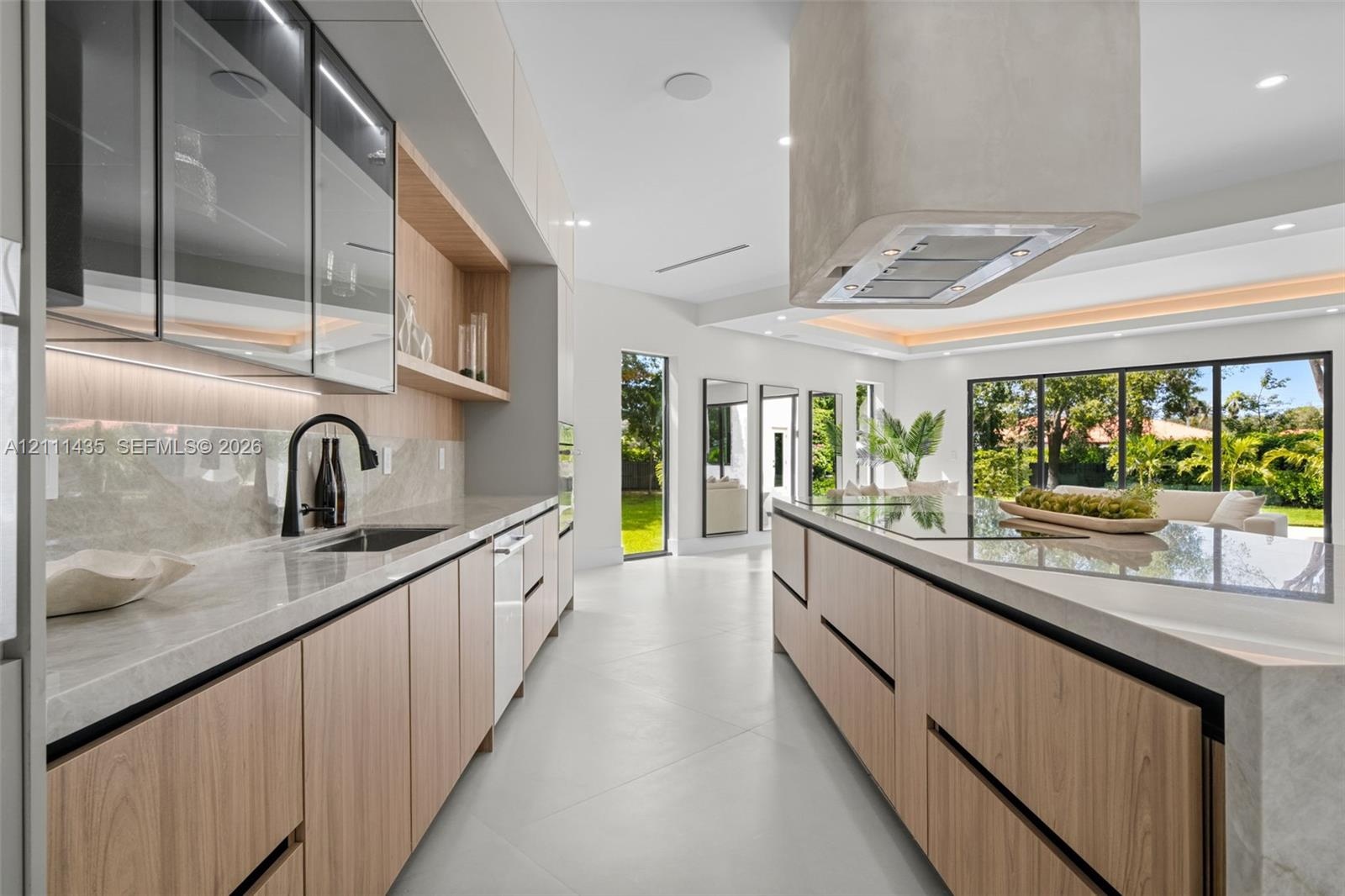 Kitchen featuring light wood-finish cabinetry, stone countertops, integrated under-cabinet lighting, a contemporary ceiling-mounted range hood, and la