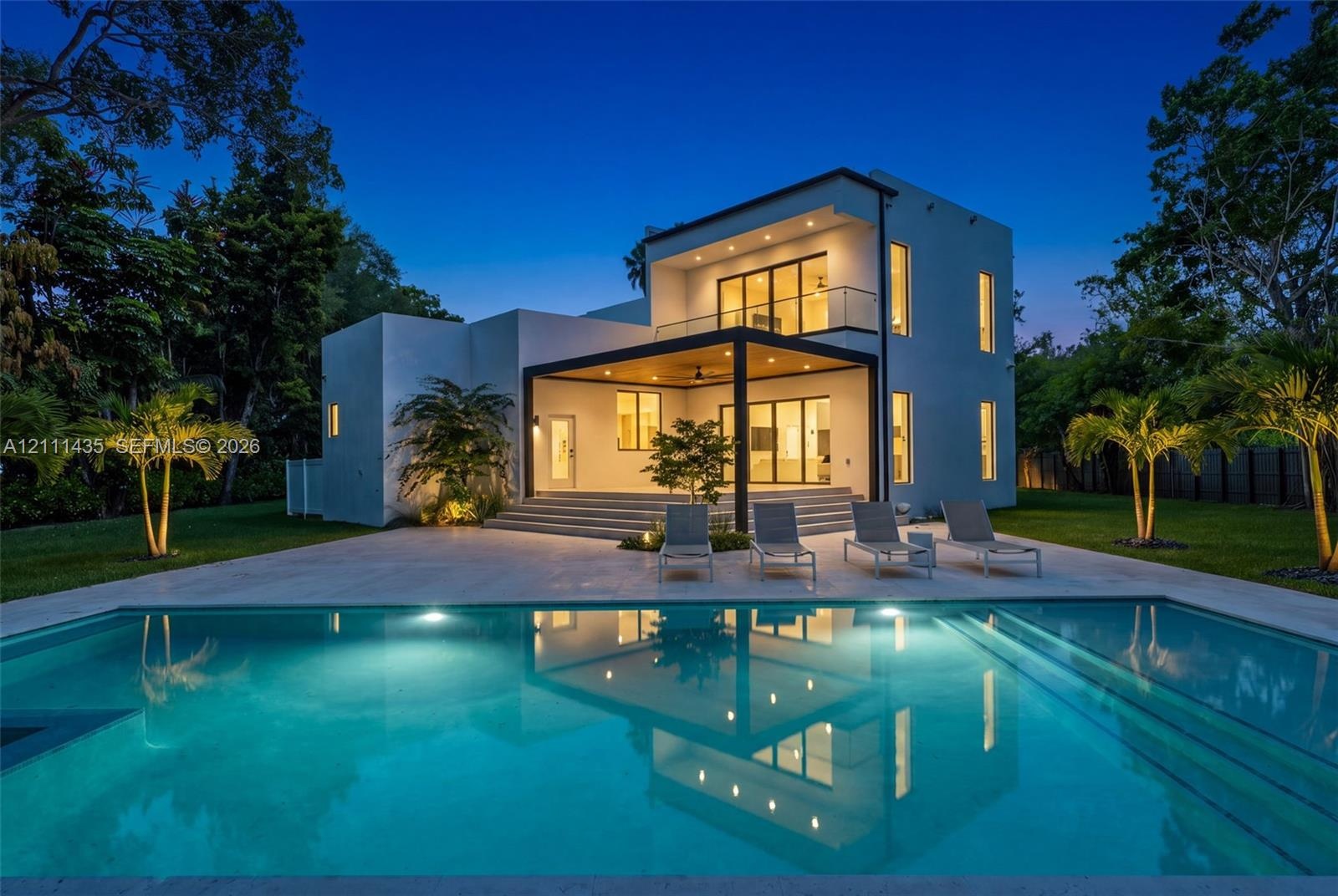 Modern two-story residence featuring a smooth stucco exterior, a covered patio with recessed lighting, a second-level balcony with a glass railing, an