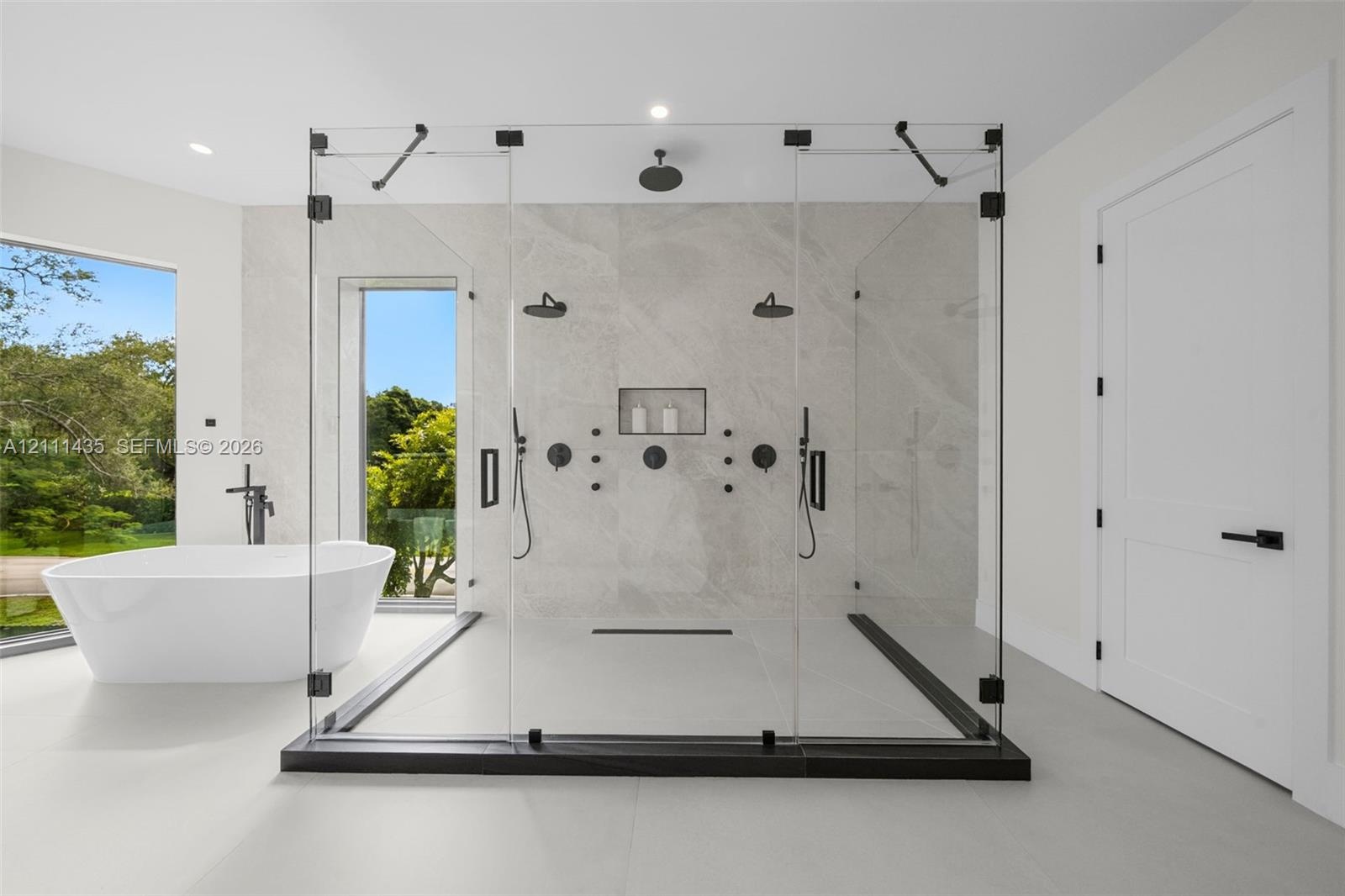 Walk-in glass-enclosed shower featuring dual shower heads, a built-in recessed niche, and stone-finish wall tile, paired with a freestanding soaking t