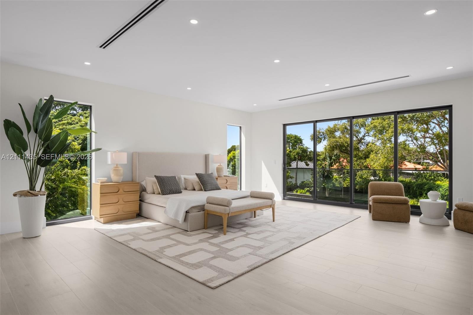 Spacious interior featuring light-toned wood-finish flooring, recessed lighting, full-height windows, and floor-to-ceiling sliding glass doors with da