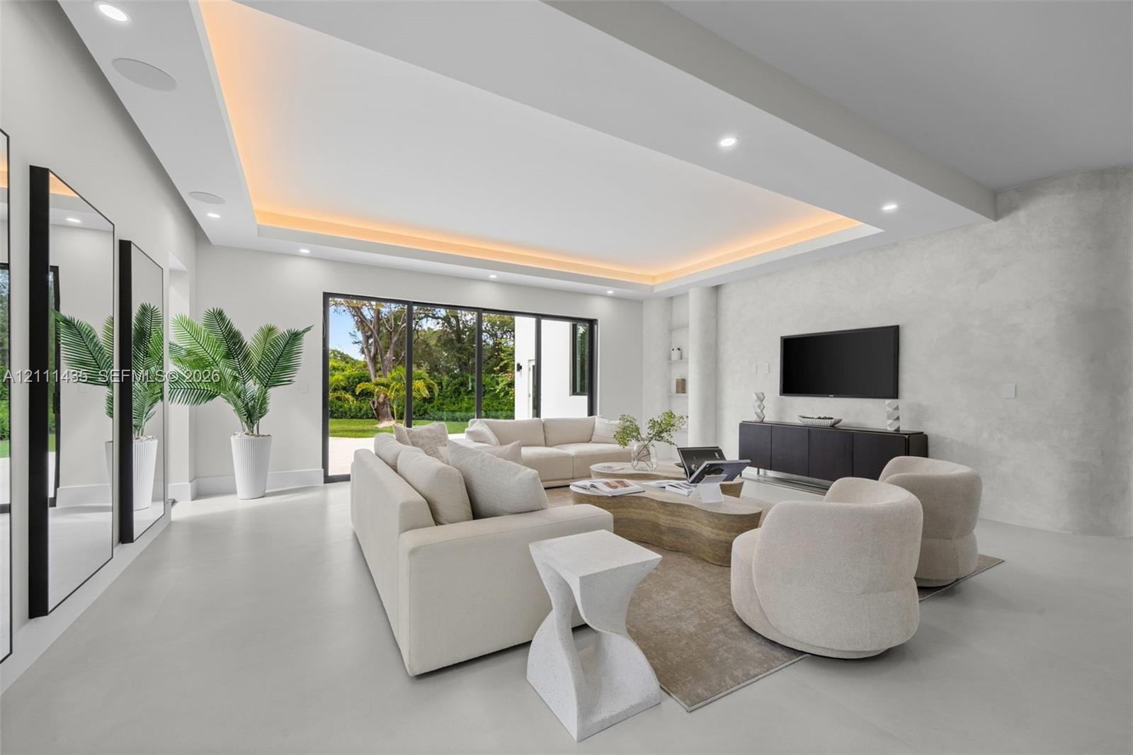 Living area featuring a coffered ceiling with integrated cove lighting, recessed ceiling lights, a textured stone-finish accent wall, and multi-panel 