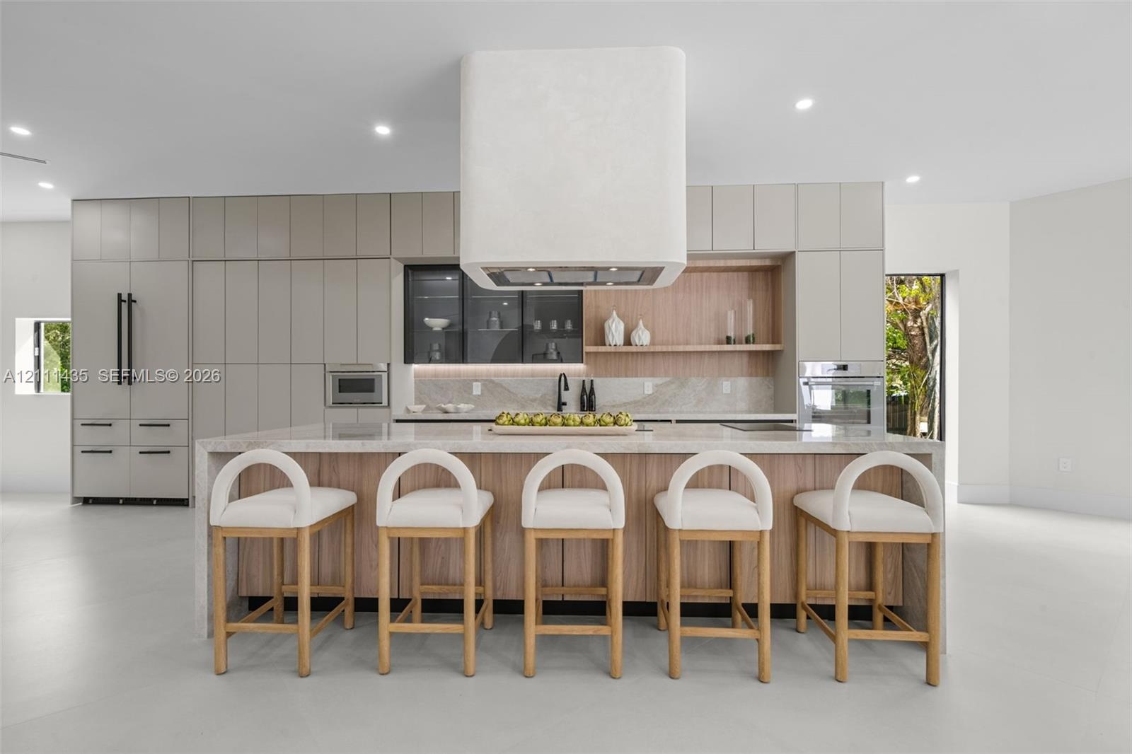 Kitchen featuring a waterfall-edge island, custom cabinetry, integrated high-end appliances, a stone-finish backsplash, and a floating range hood