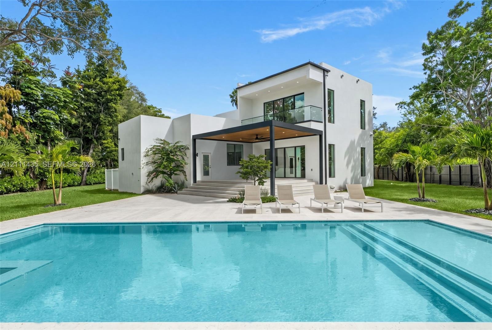 Modern two-story residence featuring a smooth stucco exterior, expansive concrete patio, built-in swimming pool with step entry, and a covered pavilio
