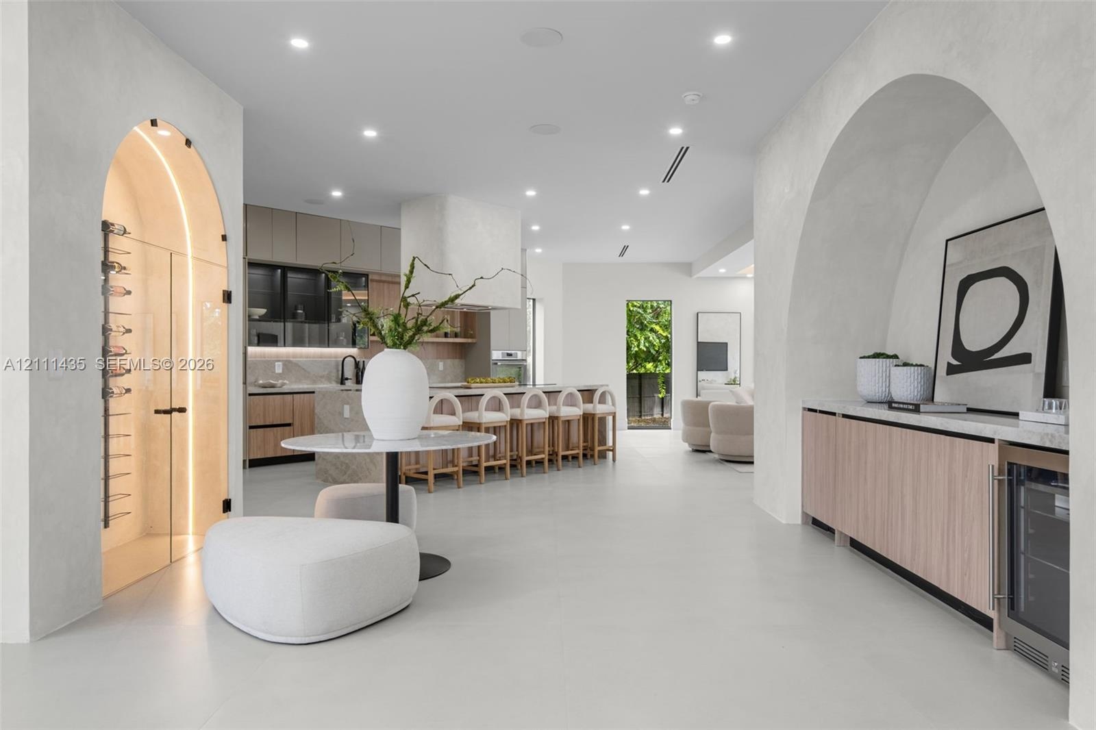 Open-concept floor plan featuring arched architectural entryways, a climate-controlled glass wine cellar, custom light wood cabinetry, and recessed li
