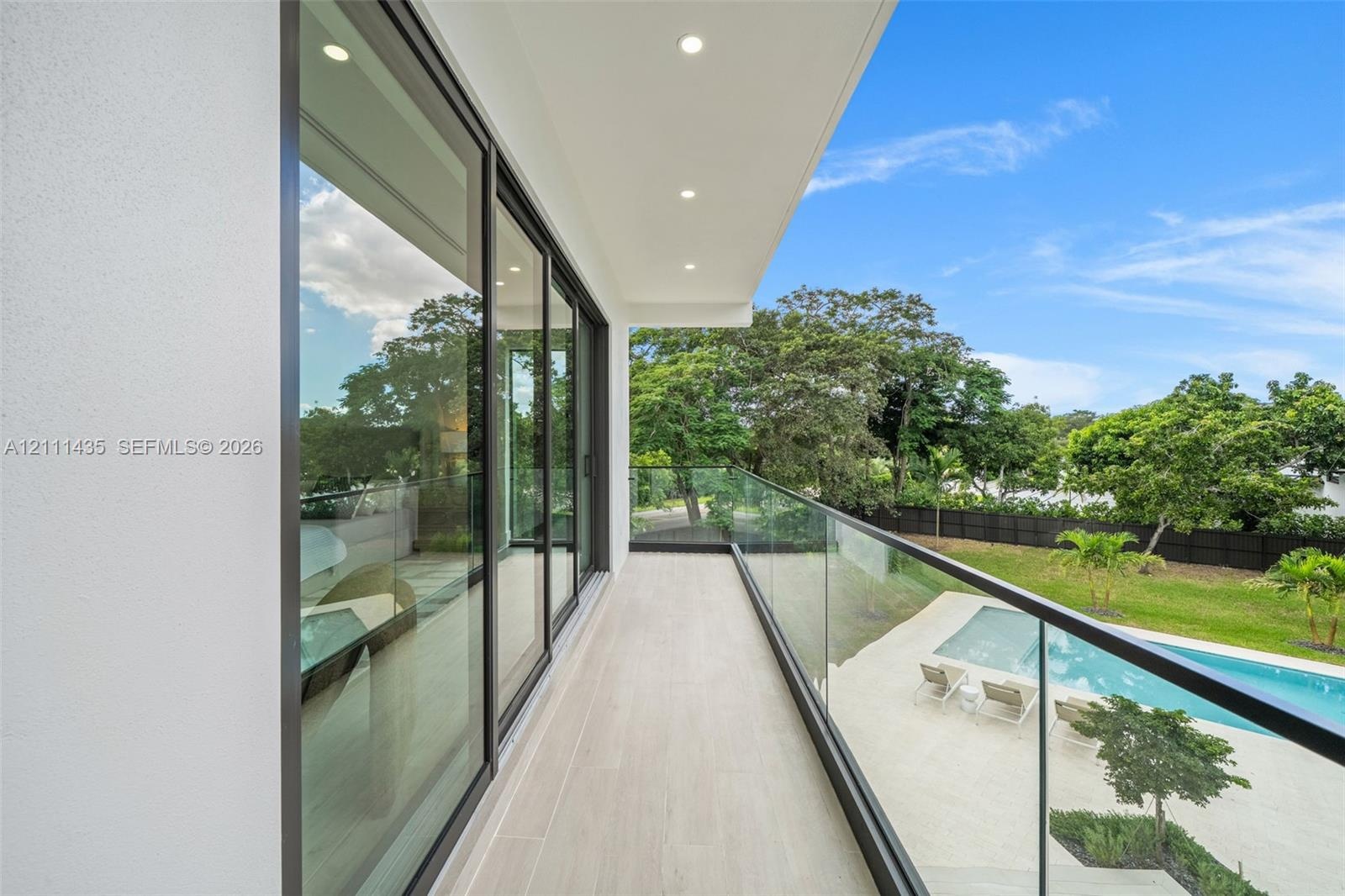Covered balcony featuring expansive sliding glass doors, frameless glass railings, recessed lighting, and tile flooring