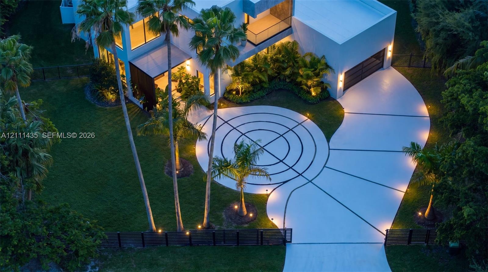 Contemporary architectural exterior featuring a geometric patterned driveway, expansive manicured lawn, multi-level structure with integrated lighting