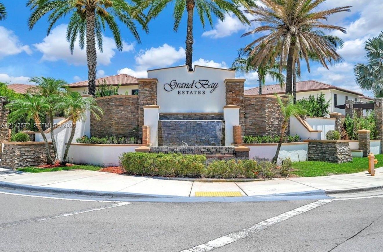 Community entrance featuring stacked-stone masonry, a built-in water feature, manicured landscaping, and mature palm trees