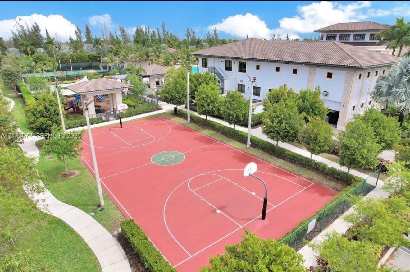 Full-sized basketball court with a red surface, dual hoops, perimeter fencing, concrete walking paths, and manicured landscaping