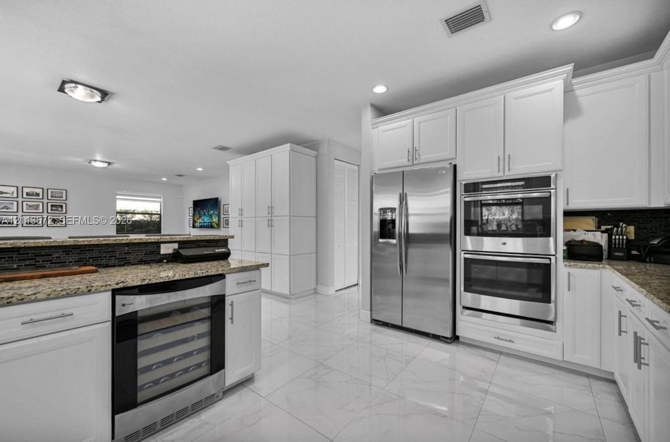 Kitchen featuring white shaker-style cabinetry, stainless steel side-by-side refrigerator, built-in double wall oven, integrated wine refrigerator, an