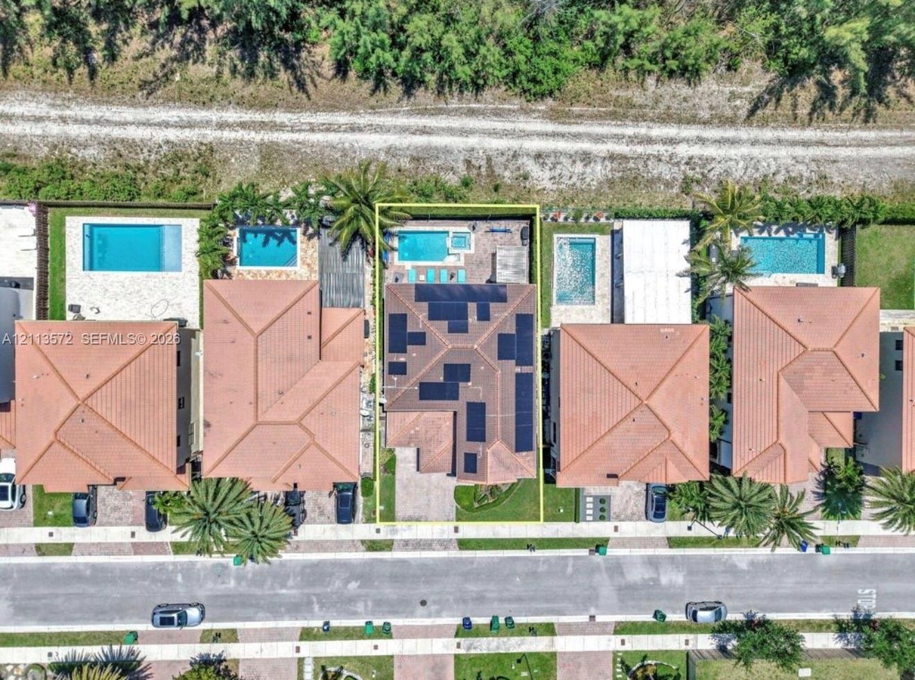 Aerial perspective of property featuring a tile roof with integrated solar panels, private swimming pool, spa, and paved rear patio