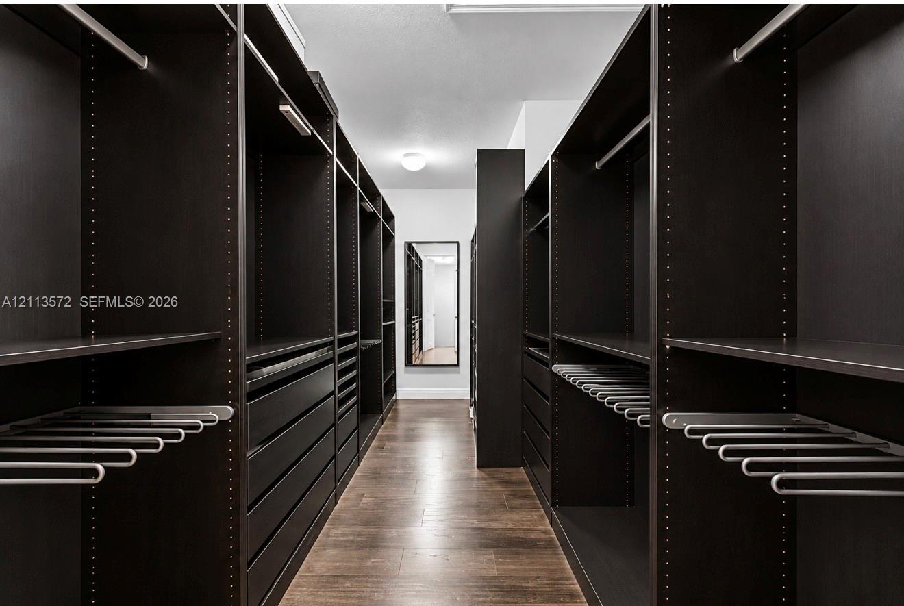 Custom walk-in storage featuring dark-finish cabinetry, built-in shelving, integrated pull-out drawers, metal garment rods, and wood-finish flooring