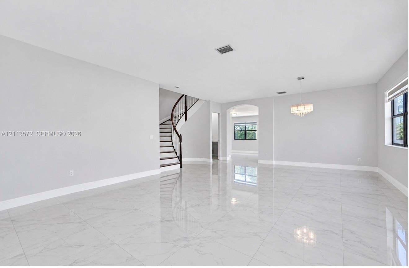 Open-concept interior featuring large-format polished stone-finish flooring, a curved staircase with a dark wood handrail, an arched entryway, and a t