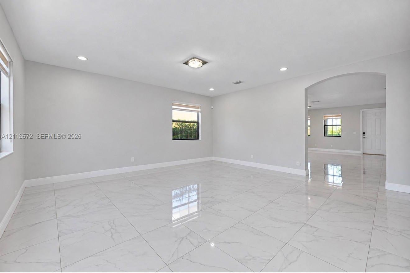 Large-format tile flooring, recessed lighting, archway architectural detailing, and neutral wall tones