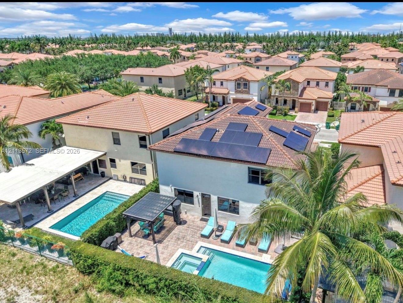 Aerial perspective featuring a two-story residence equipped with roof-mounted solar panels, a rectangular swimming pool, a spillover spa, a stone-pave