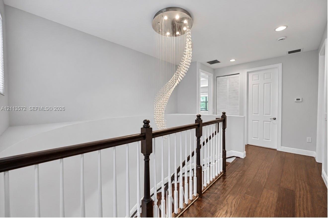 Spiral crystal chandelier with recessed ceiling lighting, wood-finish flooring, and a two-tone railing featuring a dark wood handrail and white balust