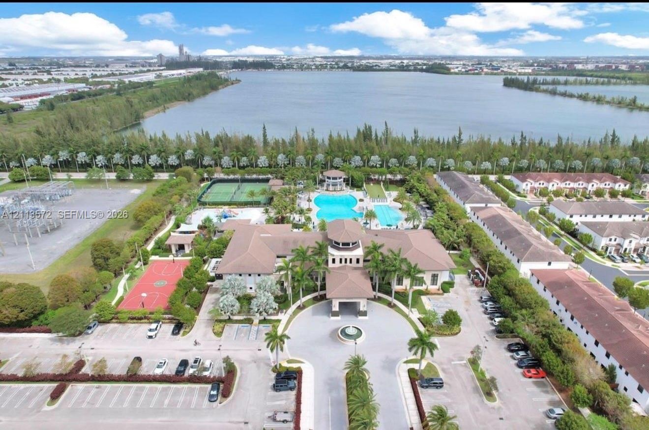 Aerial perspective of the community center featuring a swimming pool, tennis court, basketball court, and central fountain, situated alongside a lake
