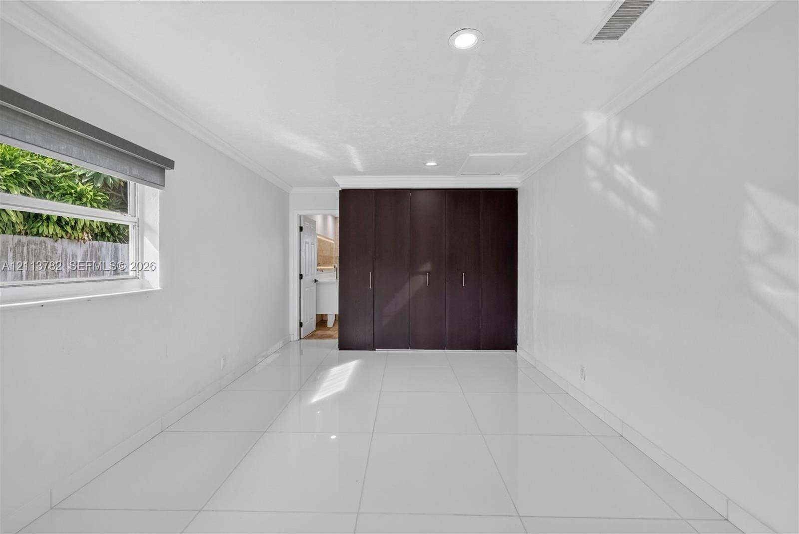 Neutral-toned interior featuring large-format white tile flooring, crown molding, recessed lighting, and floor-to-ceiling built-in cabinetry with dark