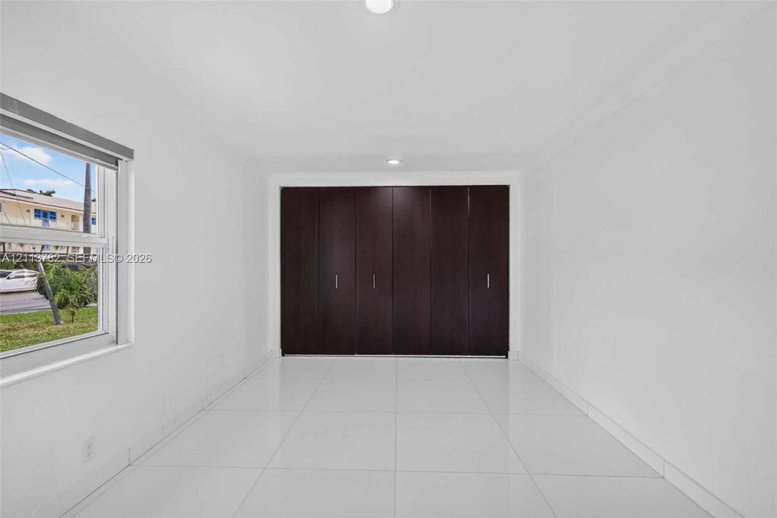 Interior space featuring large-format white tile flooring, recessed ceiling lighting, and floor-to-ceiling built-in cabinetry with dark wood-finish pa