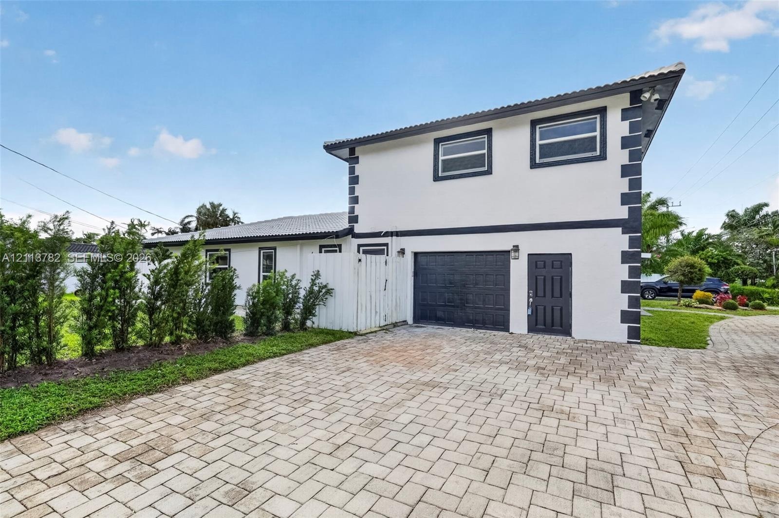 Two-story exterior featuring a high-contrast facade, paver driveway, single-car garage, and perimeter landscaping