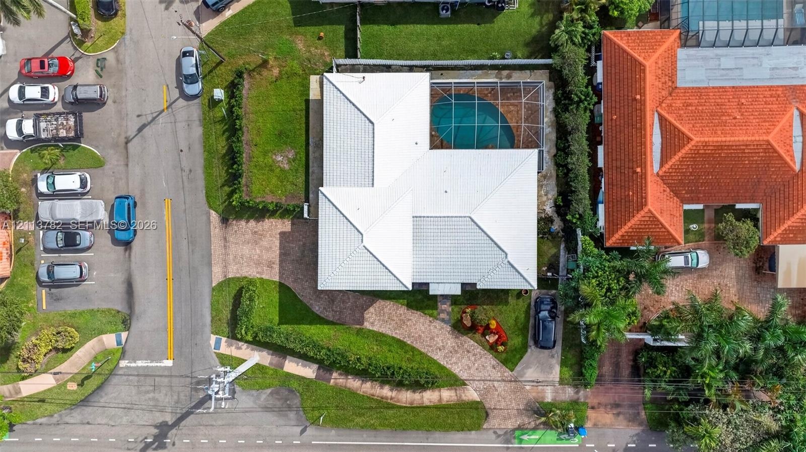 Aerial perspective featuring a light-toned hip roof, paver driveway, and a screened-in pool enclosure
