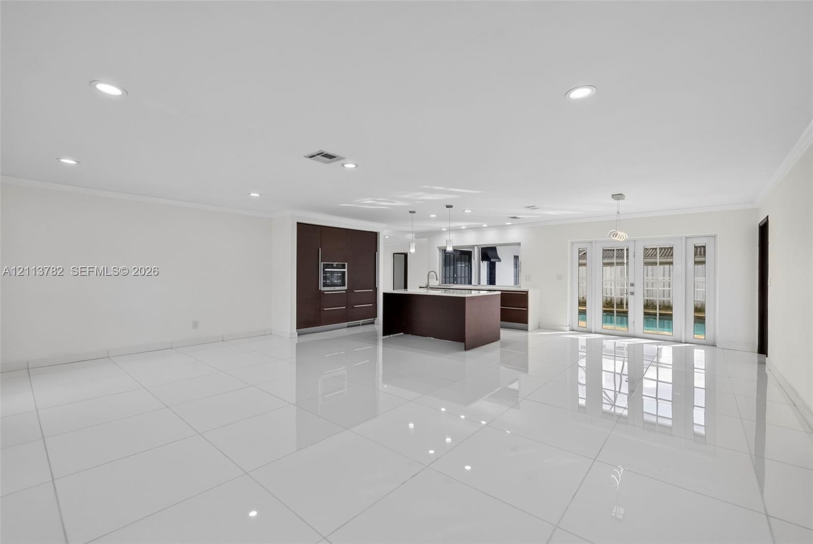 Open-concept kitchen featuring dark wood-finish cabinetry, a central island, recessed lighting, and white tile flooring throughout, accented by French