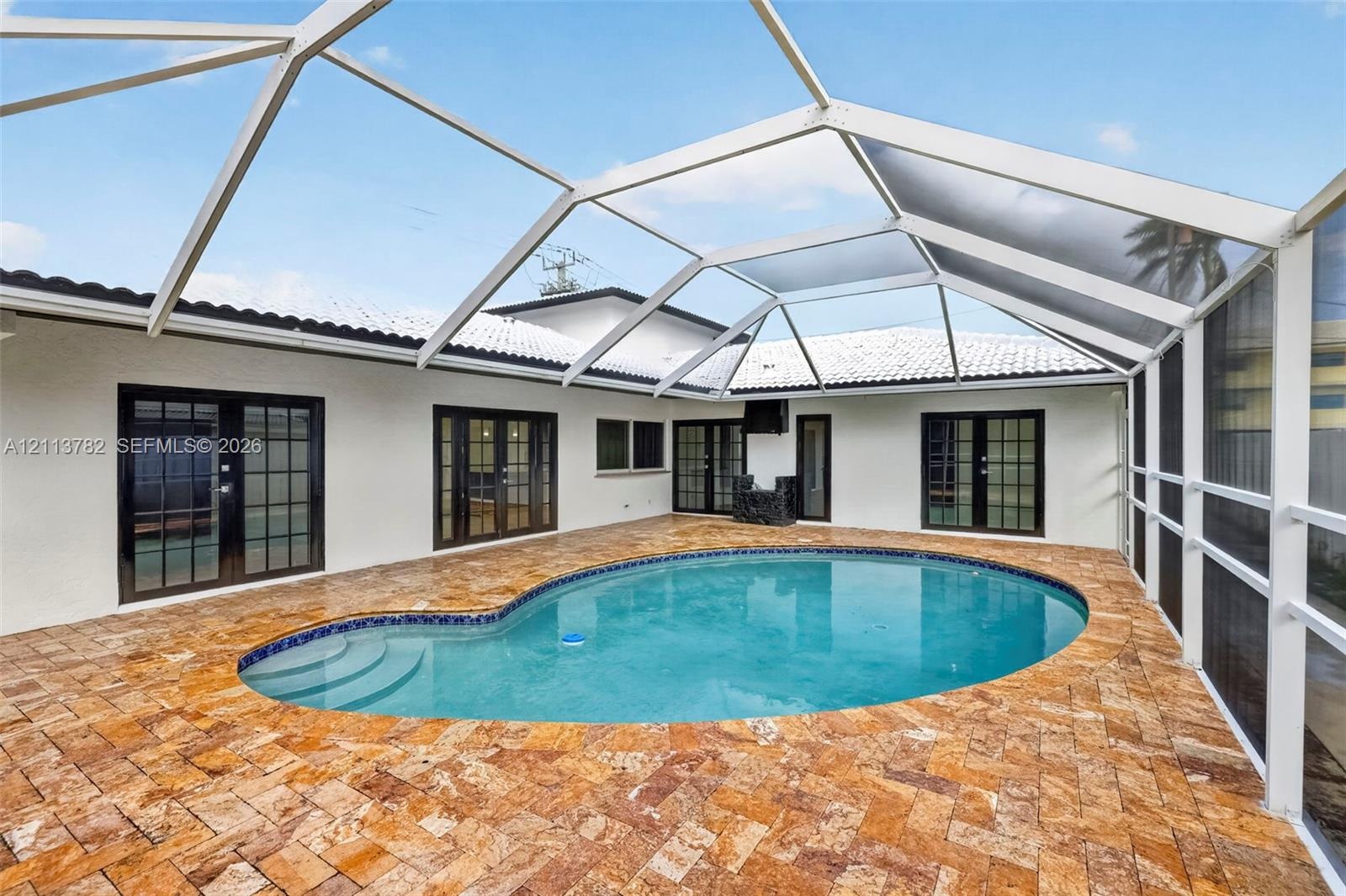Screened-in patio featuring a custom-shaped pool, natural stone paver deck, multiple glass-paned French doors, and a vaulted enclosure frame