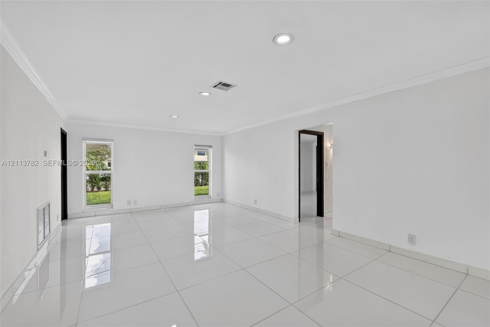 Bright living area featuring large-format polished tile flooring, recessed lighting, crown molding, and dual windows