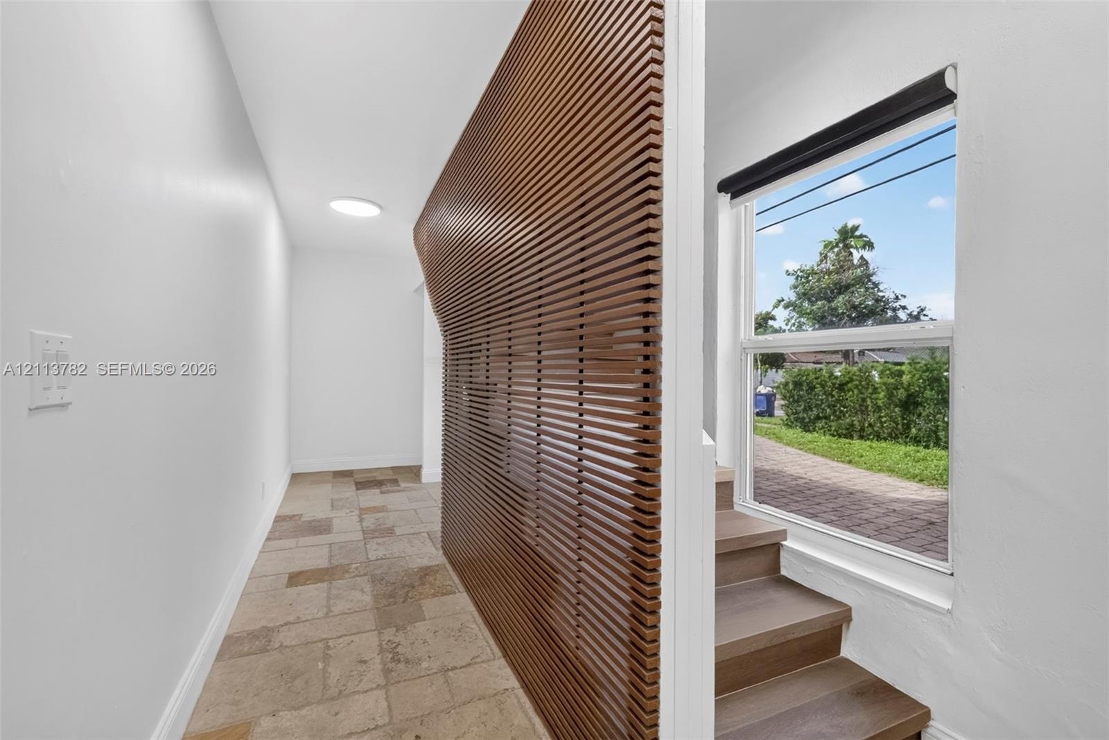 Interior featuring a curved slat-wood wall partition, large-format stone tile flooring, and stairs with wood-finish treads beneath a single-hung windo
