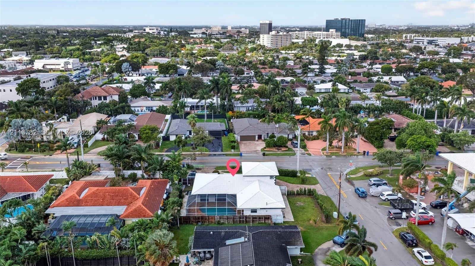 Aerial perspective featuring a white-roofed residence with a screen-enclosed pool, perimeter fencing, and established palm trees in a residential neig