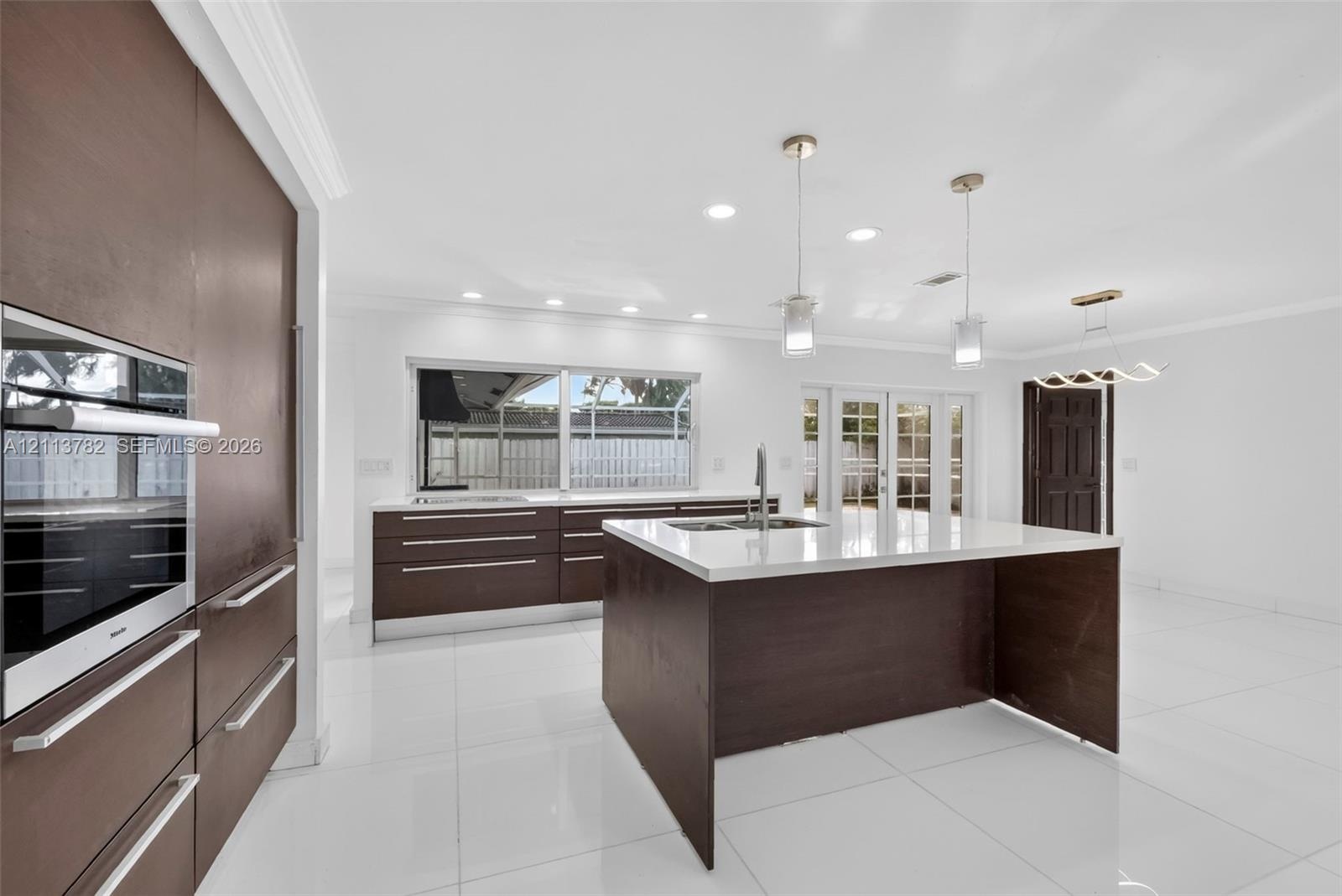 Kitchen featuring flat-panel cabinetry, a central island with a solid-surface countertop, recessed ceiling lighting, pendant light fixtures, and polis