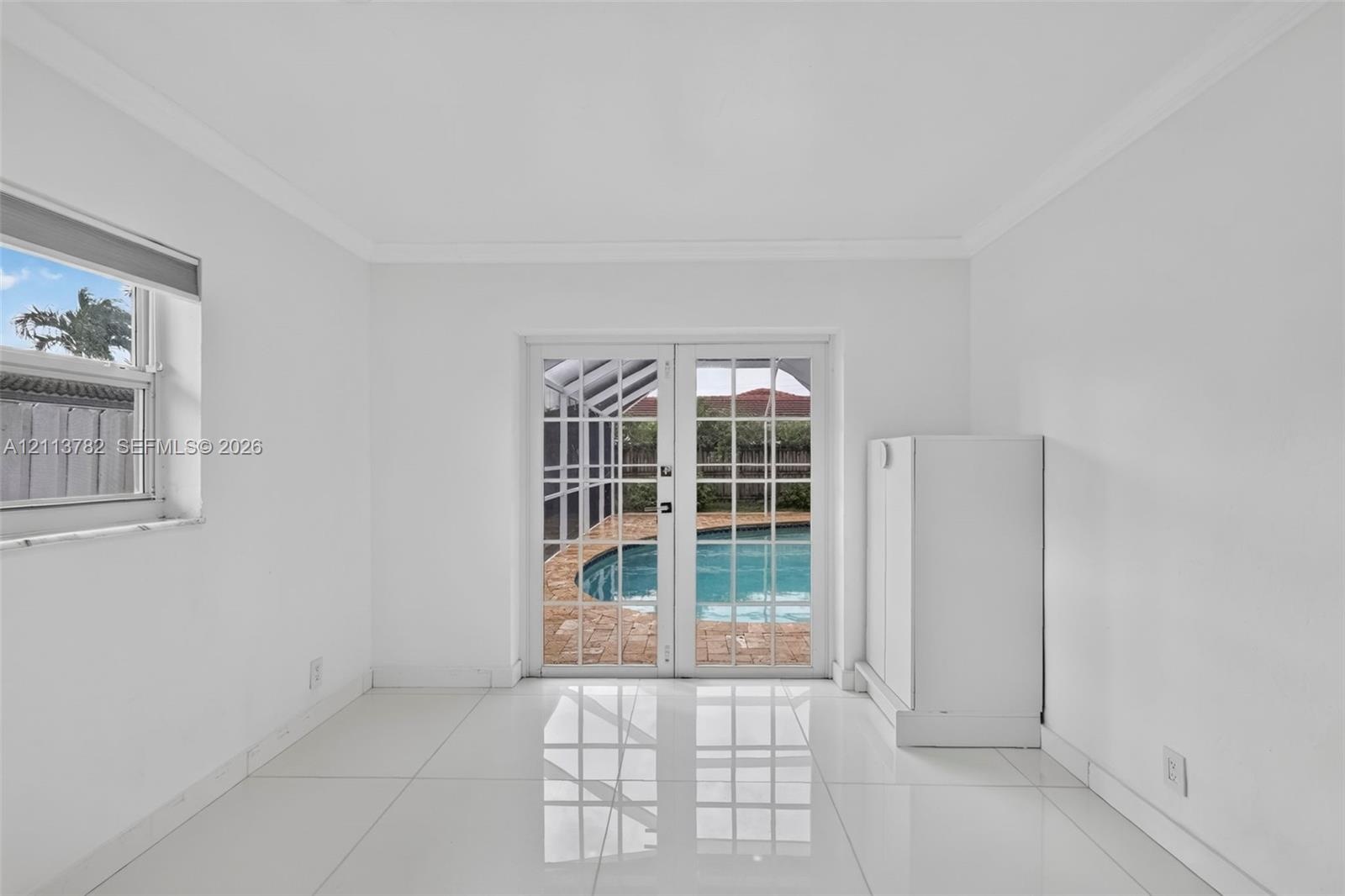 Interior space featuring white tile flooring, crown molding, double French doors, and built-in white cabinetry, with a perspective toward a screened p