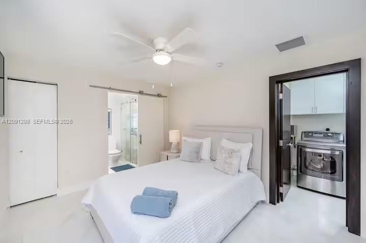 Sliding barn-style door, ceiling fan with integrated lighting, polished flooring, and a dedicated laundry area featuring built-in cabinetry and stainl