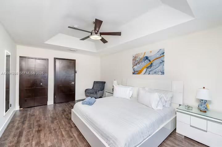 Tray ceiling featuring a central multi-blade ceiling fan, dark-finish doors, and wood-finish flooring