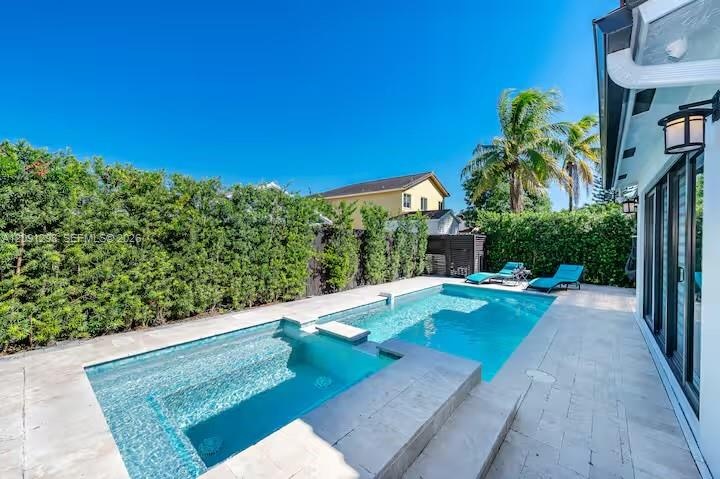Backyard featuring an inground pool with an integrated spa, stone-finish paver decking, and mature privacy hedging