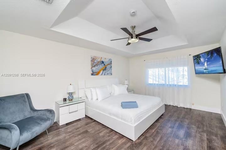 Tray ceiling featuring a central five-blade brushed-nickel ceiling fan with integrated lighting and dark wood-finish flooring